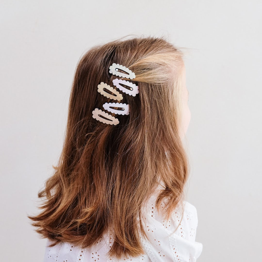 Een kind met lang, steil bruin haar draagt drie mimi & lula mini scalloped haarclipjes aan de zijkant.