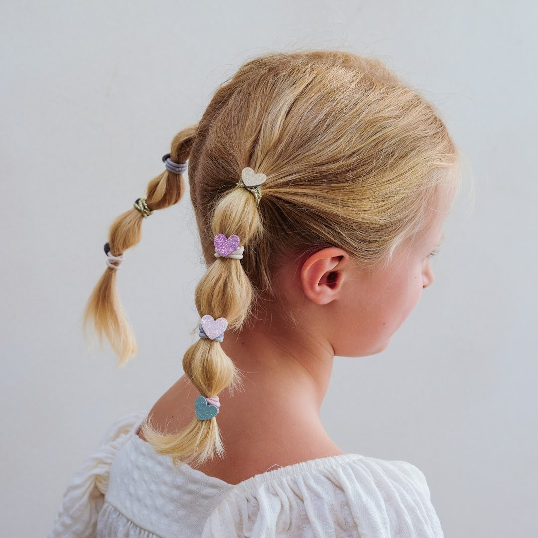 Een kind met blonde haren draagt Mimi & Lula haarelastiekjes met glitterharten in een vlecht.