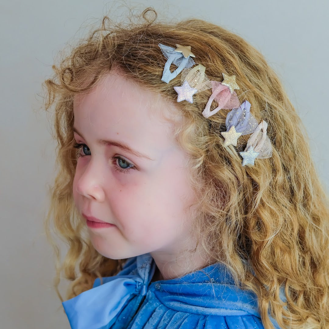Een meisje met krullend blond haar draagt mimi & lula haarclipjes met sterren in haar haar.
