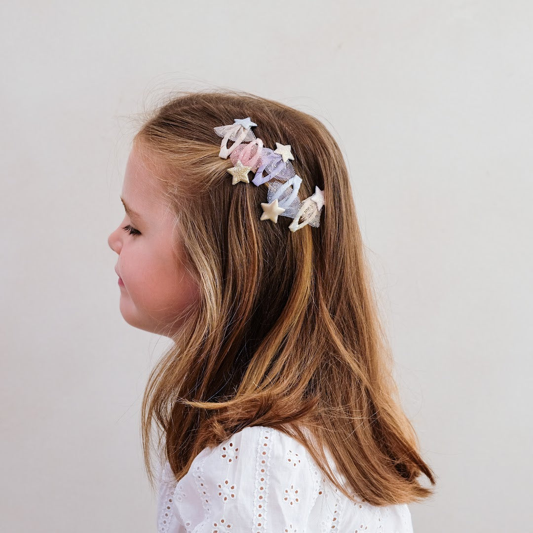 Een meisje met lang bruin haar draagt meerdere mimi & lula haarclipjes met sterren aan de zijkant van haar hoofd.