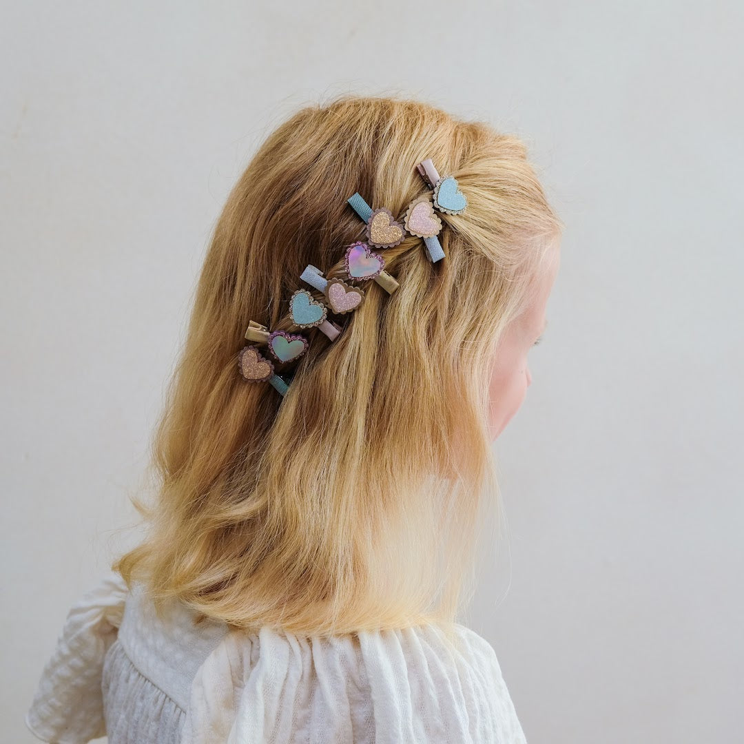 De mimi & lula haarclipjes met hartjes in het blonde haar van een kind, van achteren gezien.