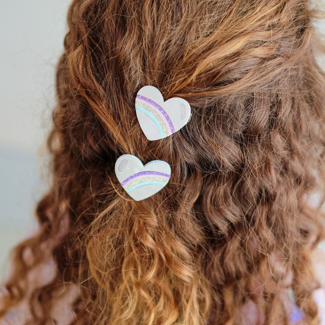 Detail van twee mimi & lula haarclipjes met regenbooghartjes in krullend haar.