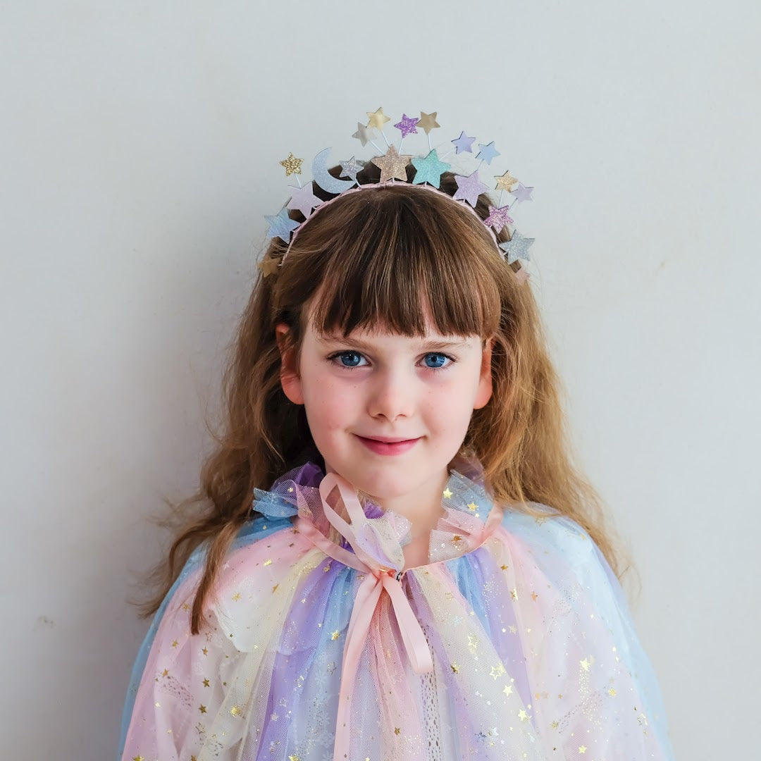 Meisje met steil haar draagt de mimi & lula hoofdband met sterren en een regenboogcape.