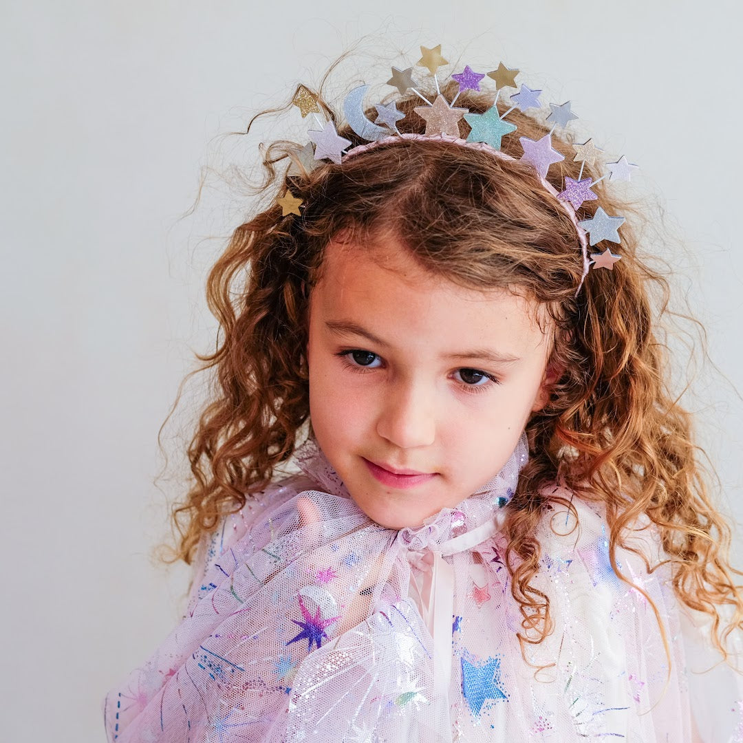Meisje met krullend haar draagt de mimi & lula hoofdband met sterren en een glittercape.