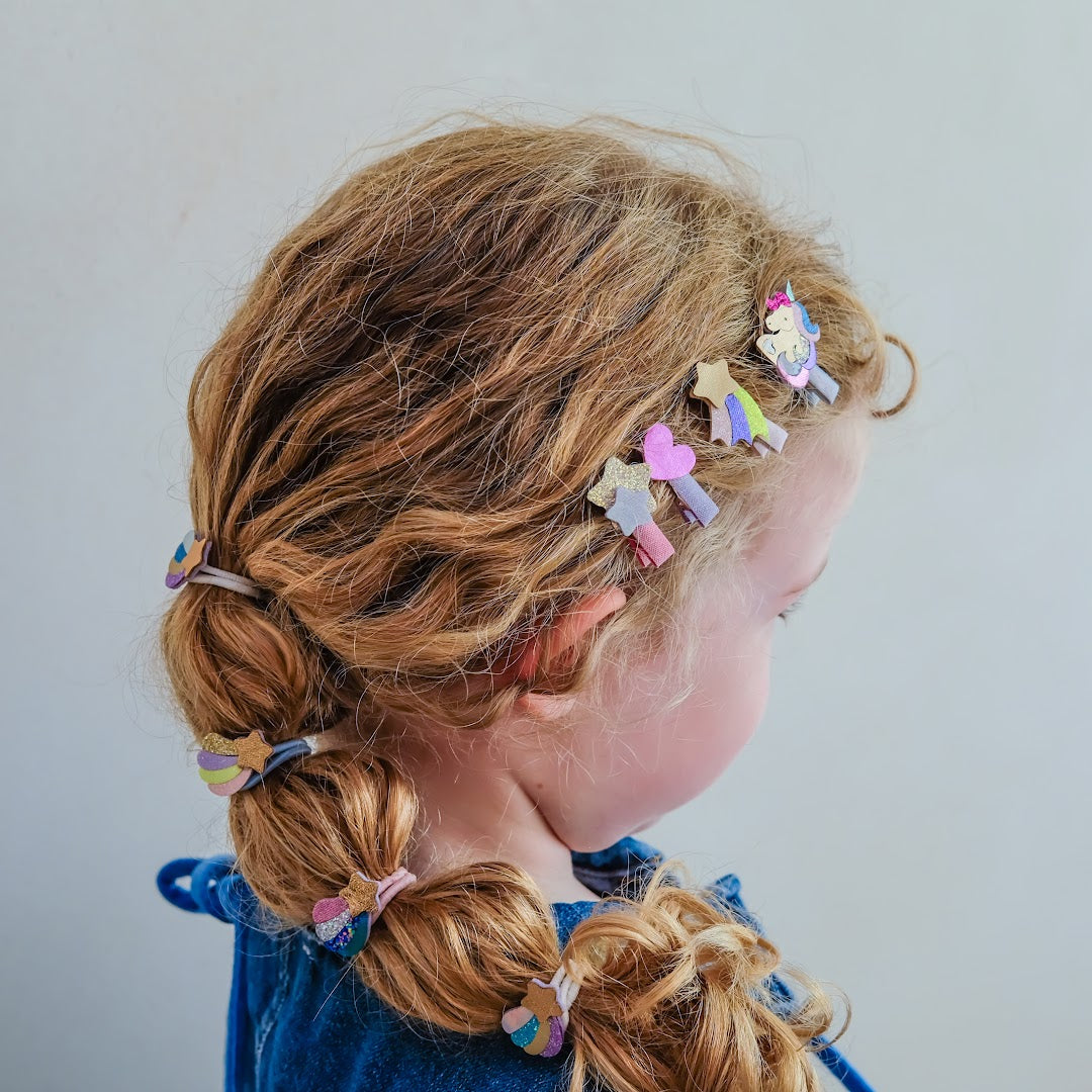 Een kind met krullend haar draagt de mimi & lula haarclipjes met eenhoorns, sterren en harten.