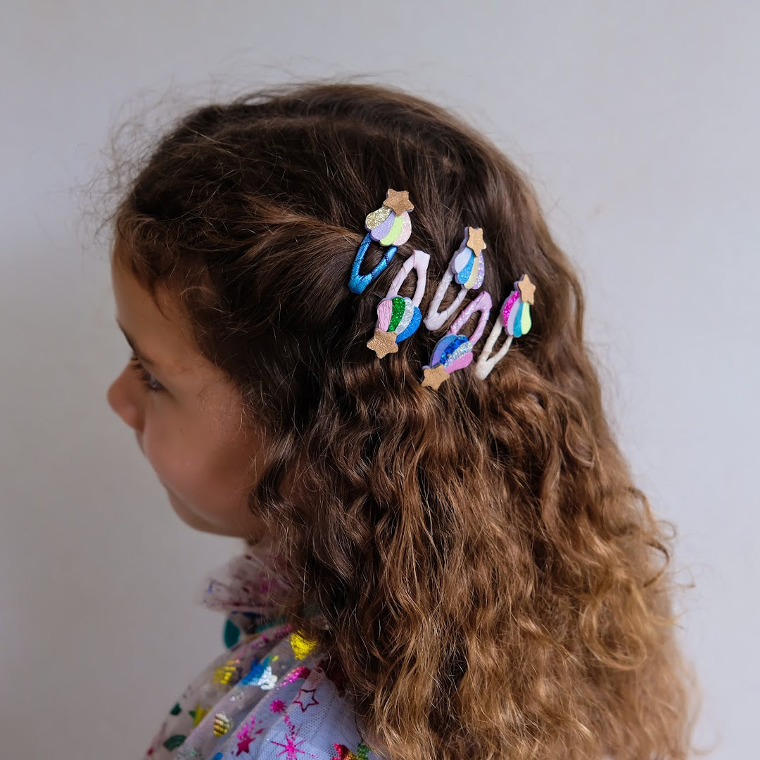Een kind met krullend haar draagt meerdere mimi & lula haarclipjes met sterren en regenboogmotieven.