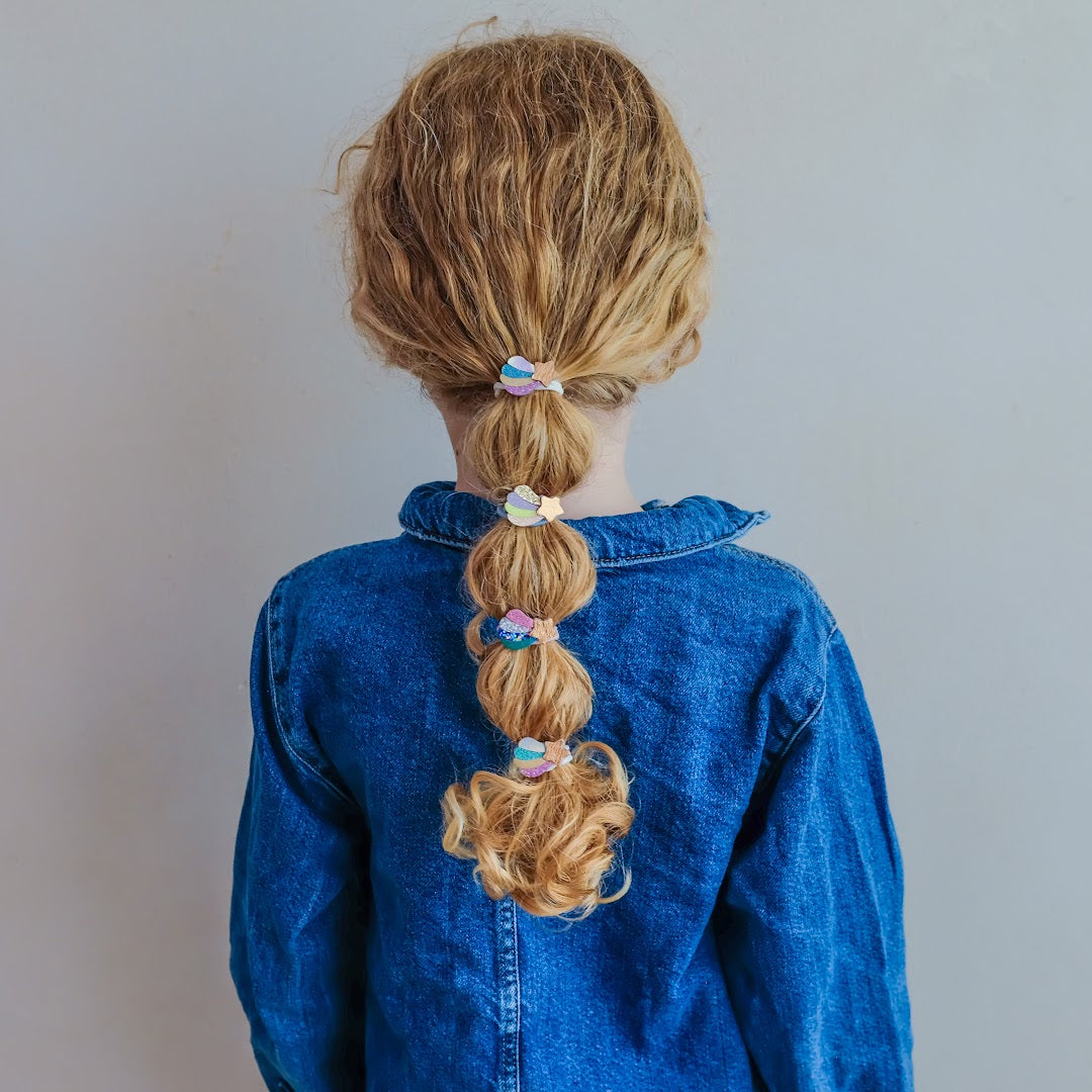 Een kind met blonde vlecht, versierd met meerdere mimi & lula haarelastiekjes met vallende sterren.