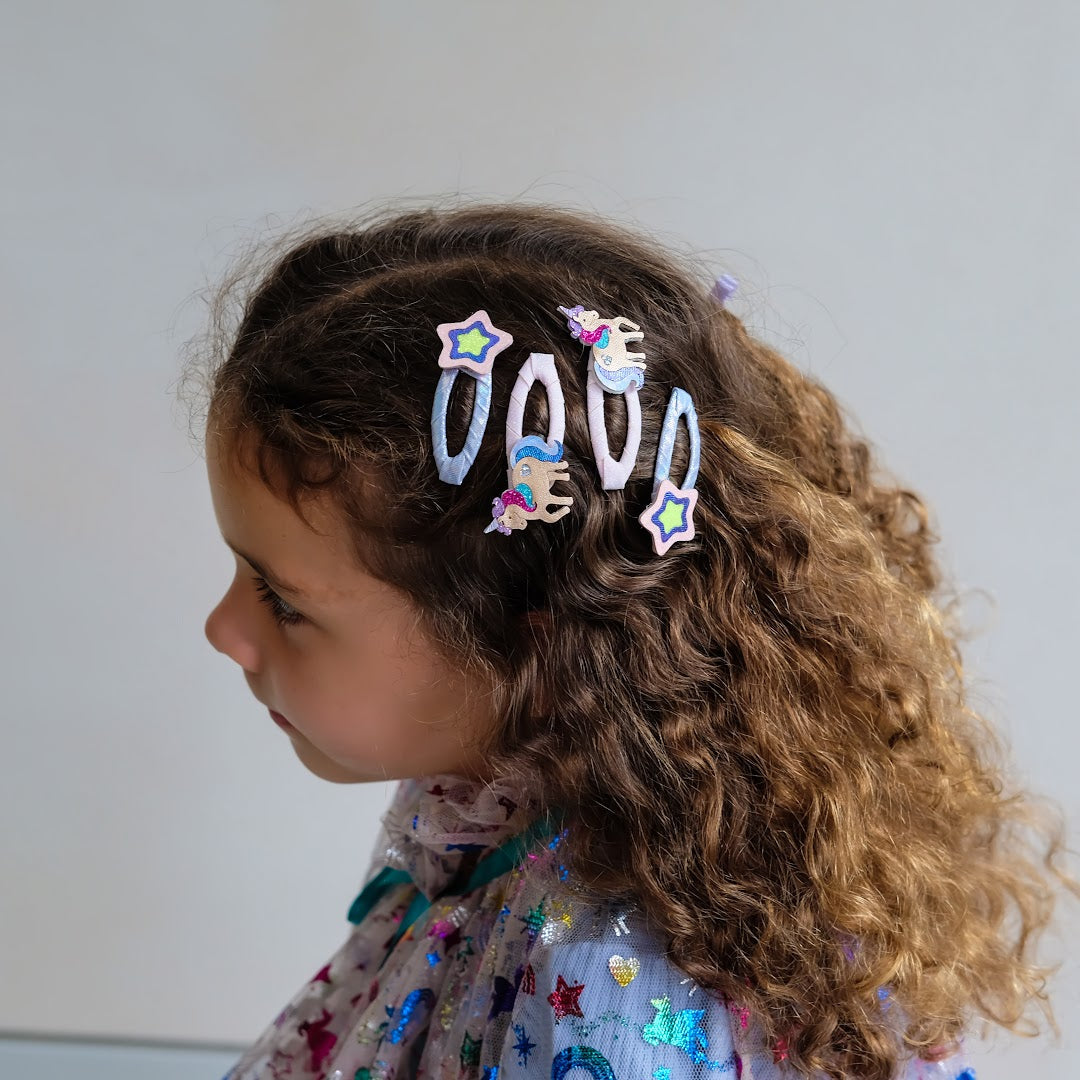 Een kind met krullend haar draagt meerdere eenhoorn en ster haarclipjes.