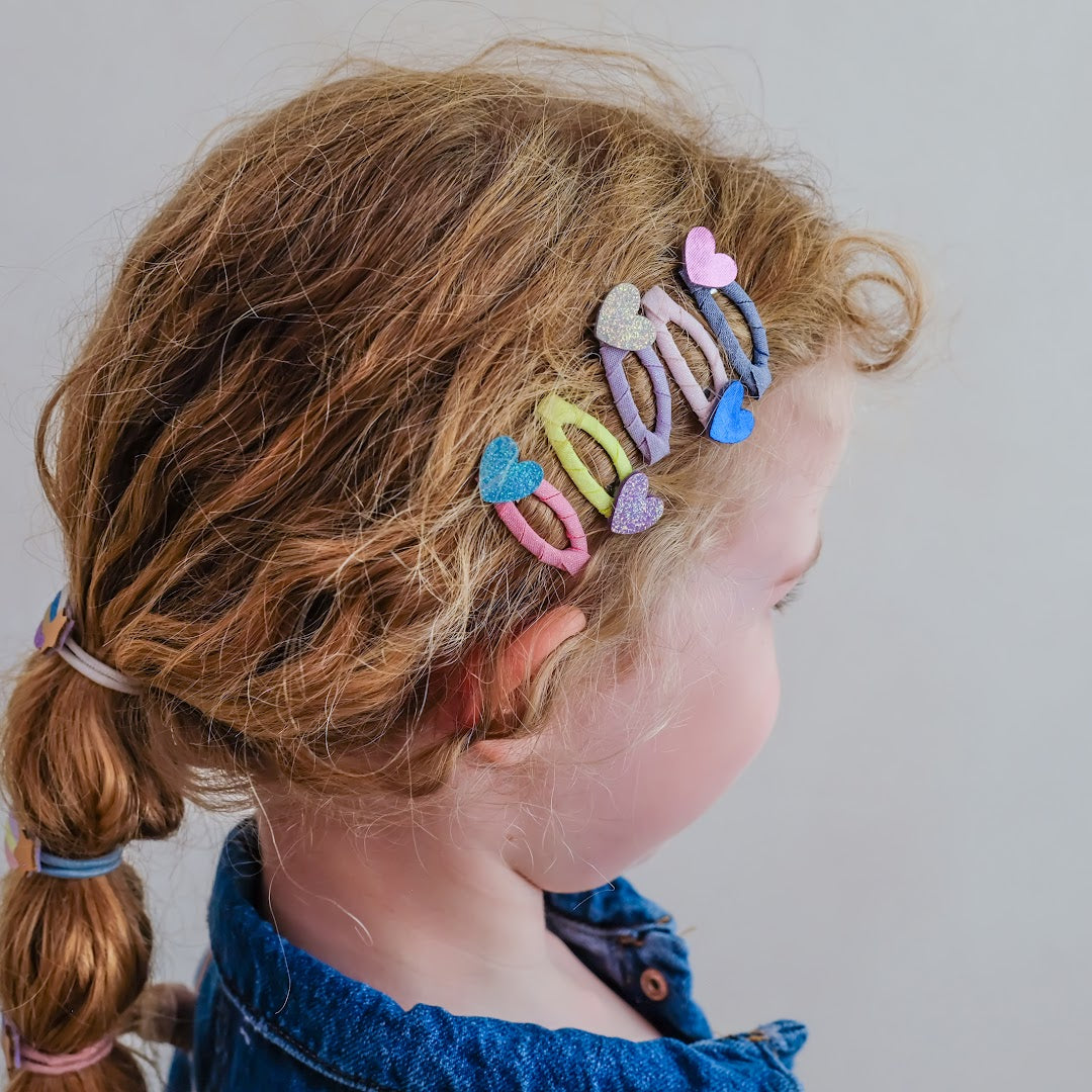 Een kind met krullend haar draagt meerdere haarclipjes met glitterharten.