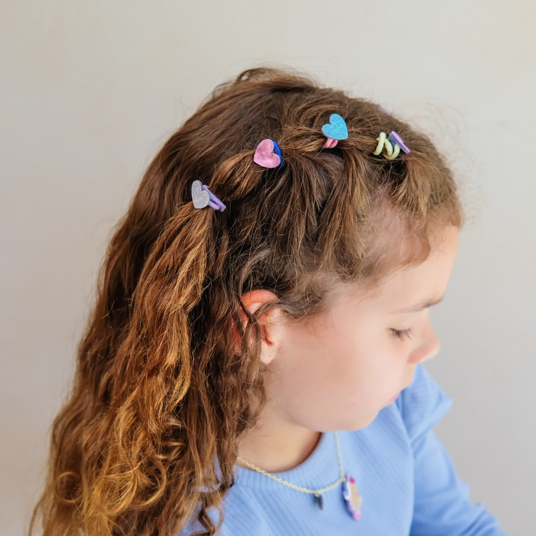 Een kind met krullend haar draagt meerdere kleurrijke haarelastiekjes met glitterharten.