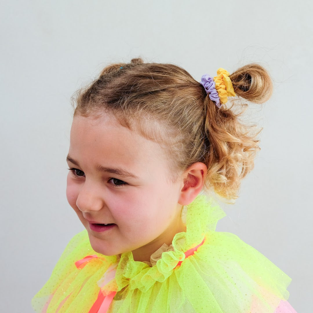 Een meisje met krullend haar en een neongele top, met twee mimi & lula haarelastieken in een knotje.