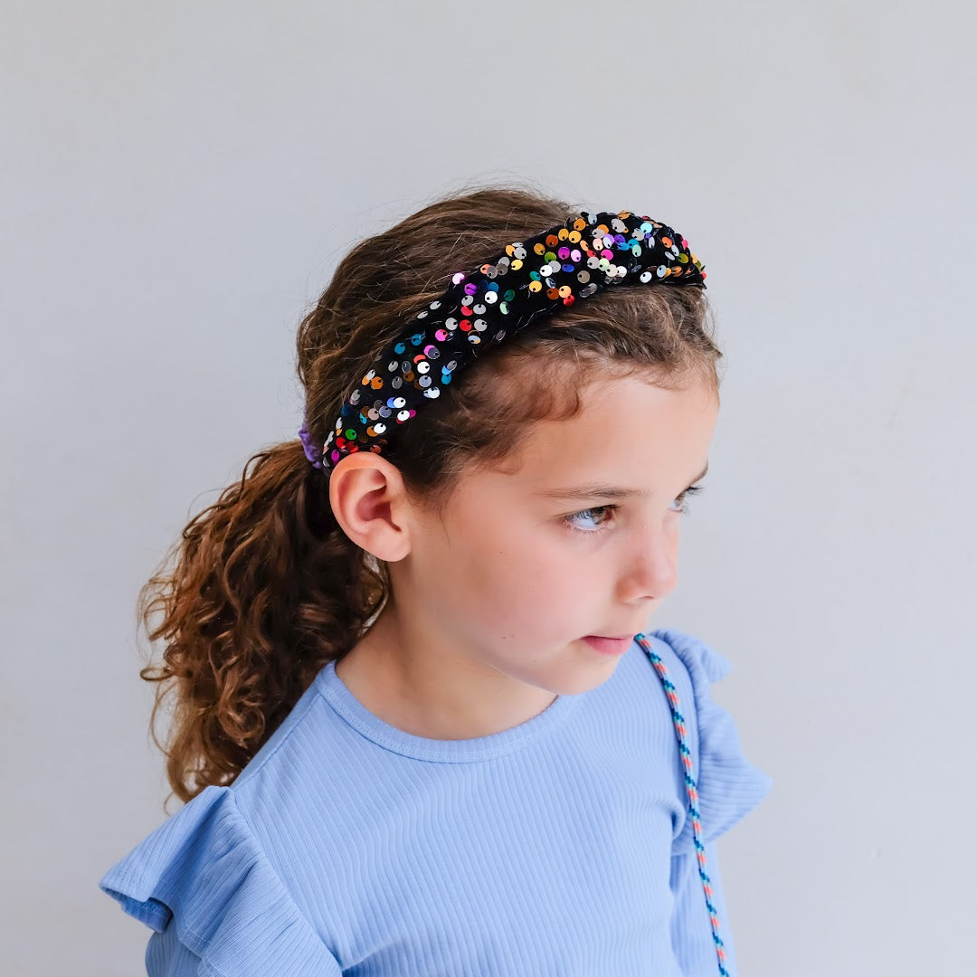 Zijaanzicht van een kind met de mimi & lula hoofdband met veelkleurige lovertjes en een lichtblauwe top.