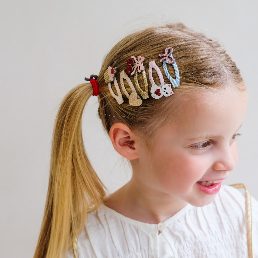 Een lachend meisje met blonde staartjes draagt mimi & lula haarclipjes in haar haar.