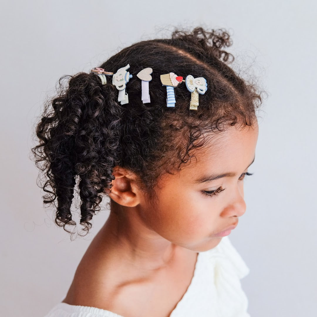 Een kind met donker, krullend haar draagt de mimi & lula haarclipjes met 'afternoon tea' thema aan de zijkant van haar hoofd.