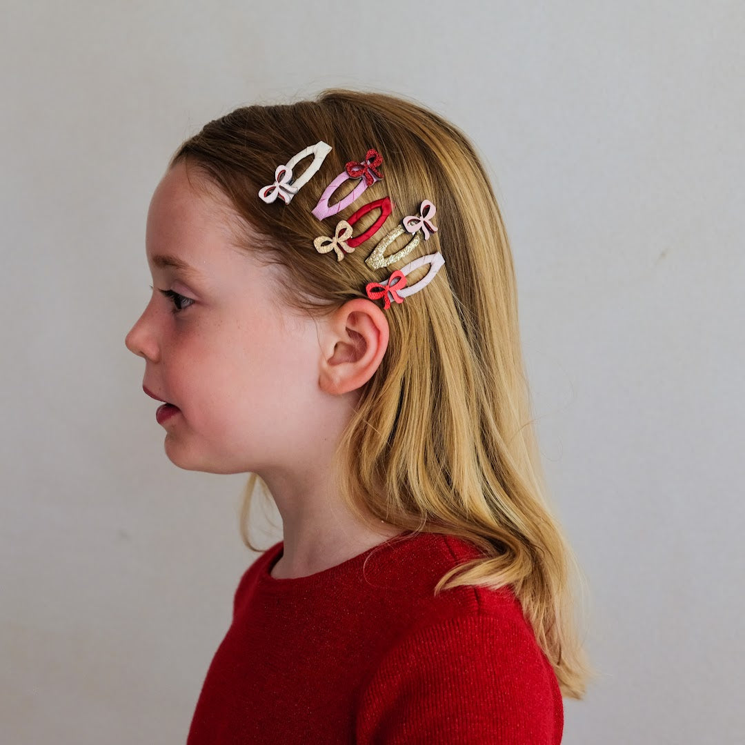 Een kind met lang blond haar draagt meerdere mimi & lula haarclipjes met strikjes.