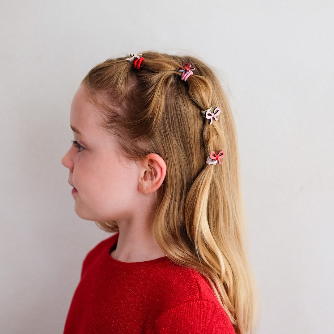 Zijprofiel van een kind met blonde vlechten, versierd met Mimi & Lula mini haarelastiekjes met strikjes.