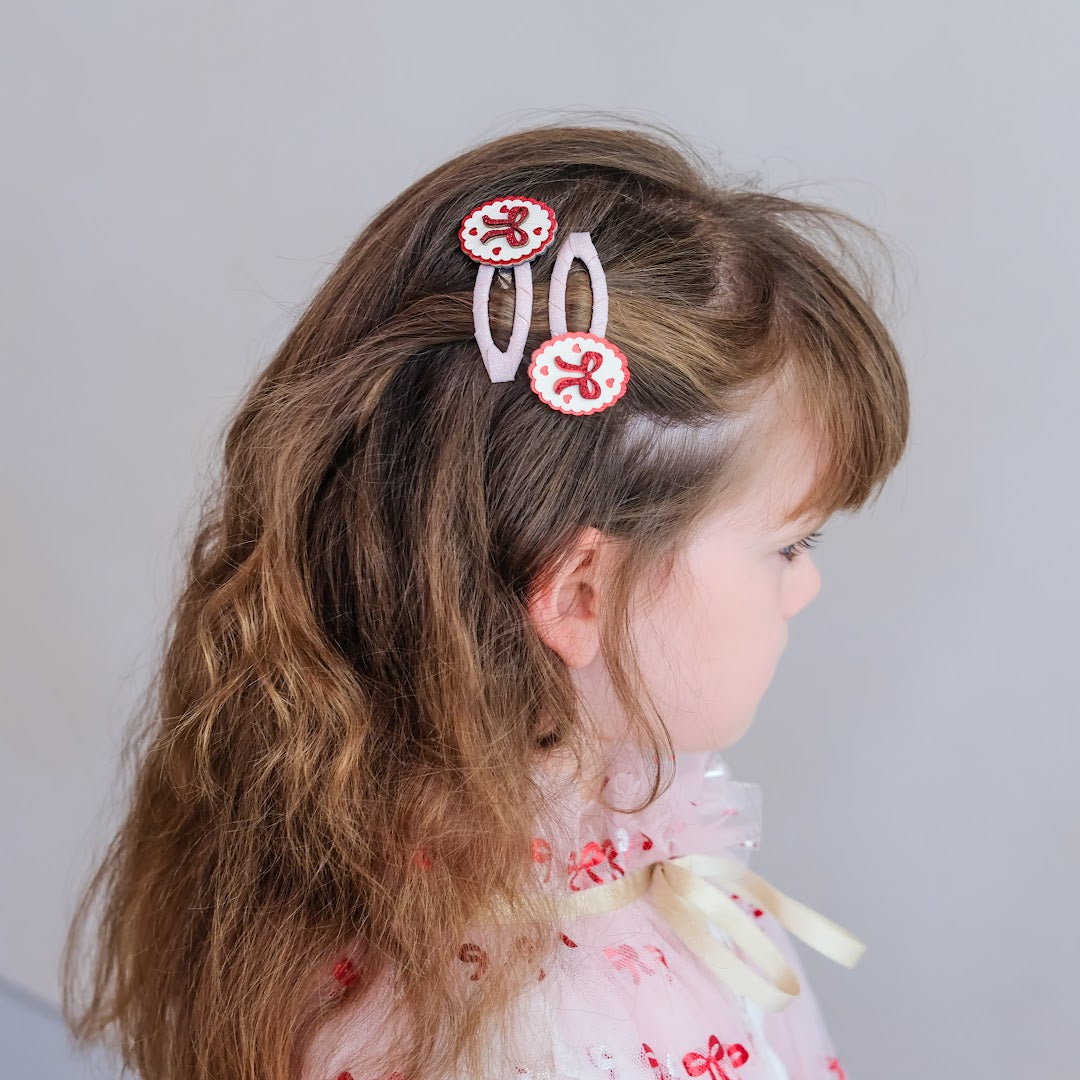 Een meisje met bruin haar draagt twee mimi & lula haarclipjes met strikjes en hartjes.