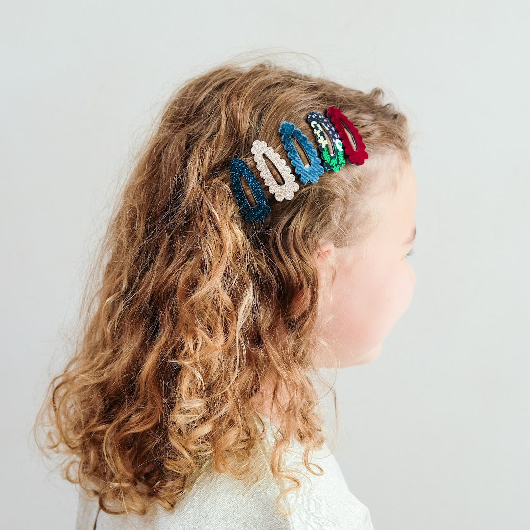 Een kind met krullend haar draagt vijf mimi & lula haarclipjes met geschulpte rand in diverse kleuren.
