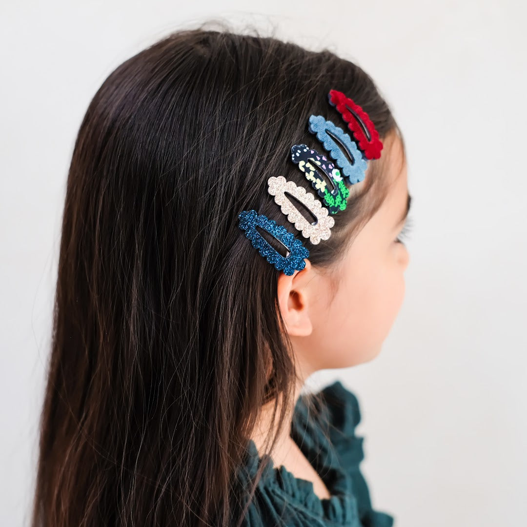 Een kind met steil donker haar draagt vijf mimi & lula haarclipjes met geschulpte rand in diverse kleuren.