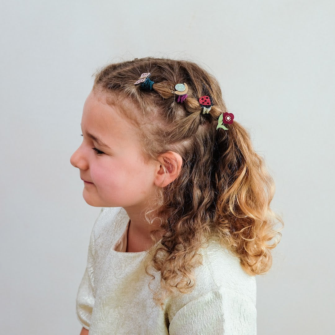 Een kind met krullend haar en vlechtjes, versierd met mimi & lula haarelastiekjes met dieren en bloemen.