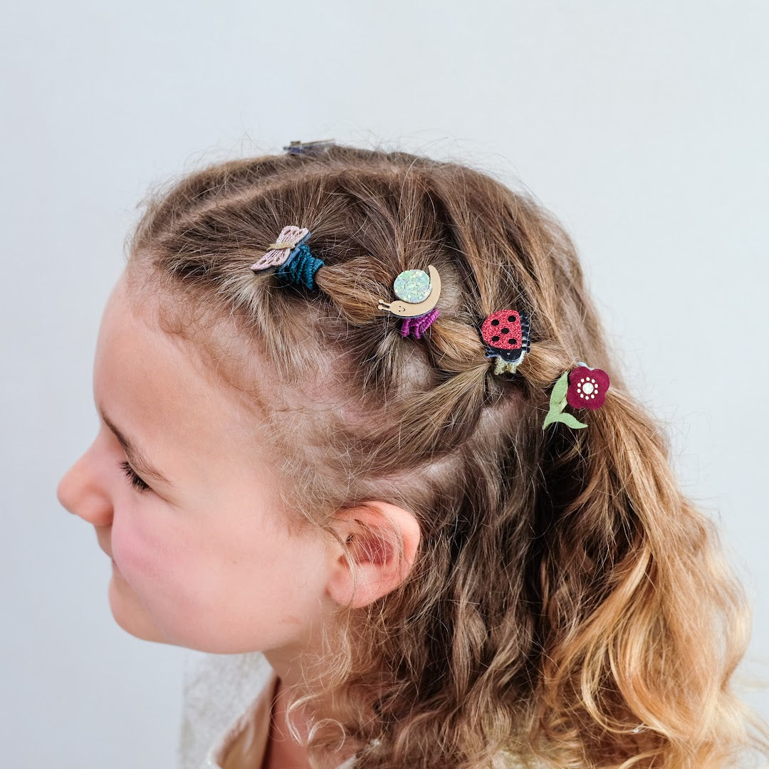 Een kind met gevlochten haar versierd met mimi & lula haarelastiekjes met lieveheersbeestjes, vlinders, slakken en bloemen.