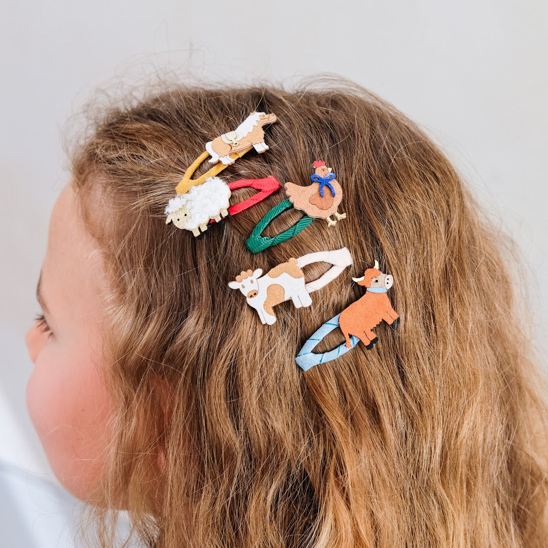 Een kind met lang haar draagt verschillende mimi & lula haarclipjes met boerderijdieren.