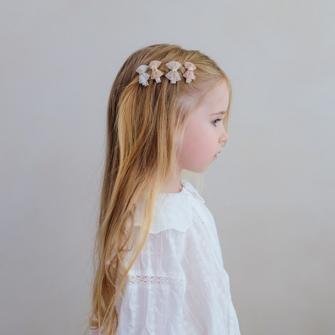 Een meisje met lang haar draagt vier mimi & lula haarclipjes met strikjes en sterren.