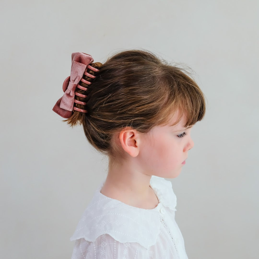 Zijaanzicht van een meisje met de mimi & lula roze fluwelen strik haarclip in opgestoken haar.