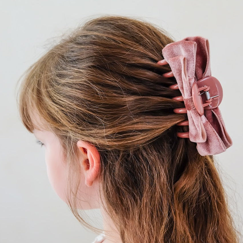 Detailfoto van de mimi & lula roze fluwelen strik haarclip in het haar van een meisje, van achteren gezien.