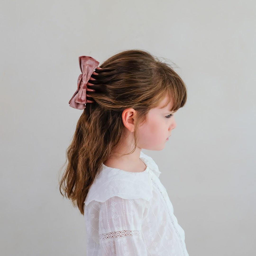 Zijaanzicht van een meisje met de mimi & lula roze fluwelen strik haarclip in half opgestoken haar.