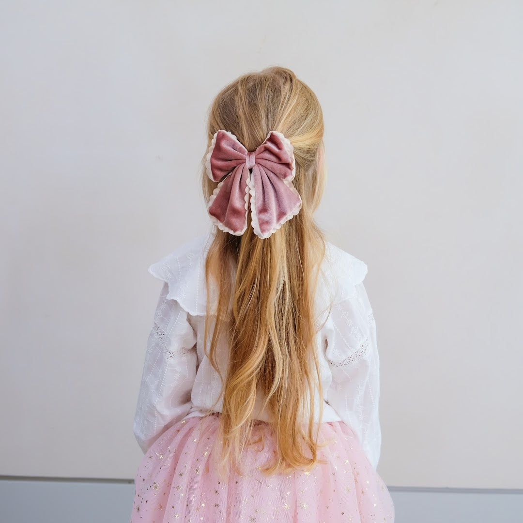 Kind met lang blond haar draagt de mimi & lula haarstrik van roze fluweel.