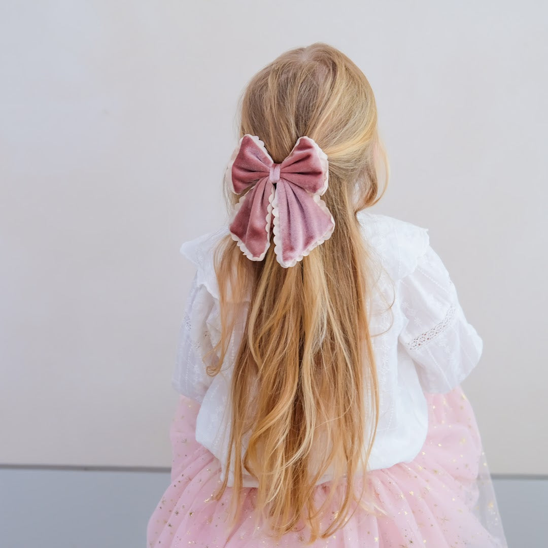 Een kind draagt de mimi & lula haarstrik van roze fluweel in lang blond haar, van achteren gezien.
