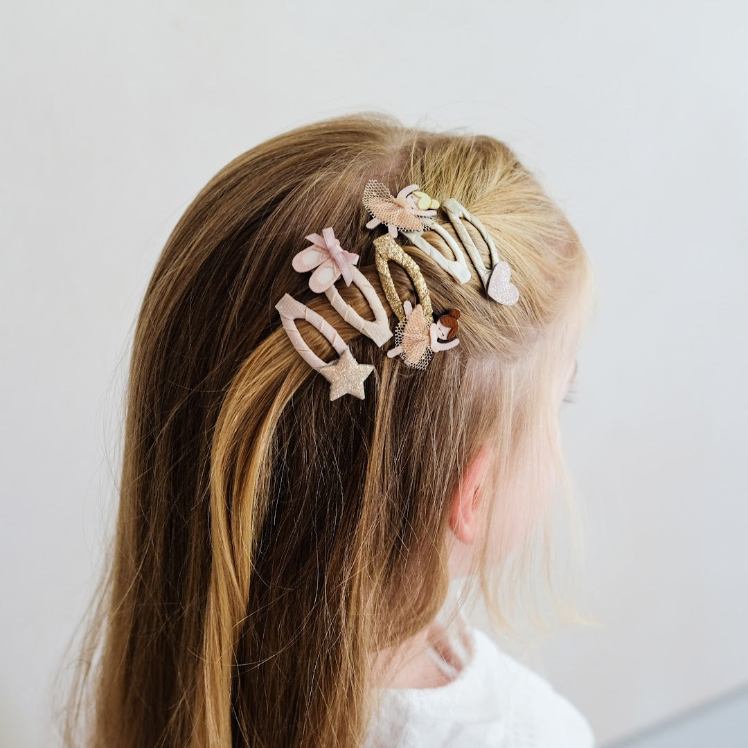 Een kind met lang blond haar draagt Mimi & Lula haarclipjes met ballerina's, een hart en een ster.