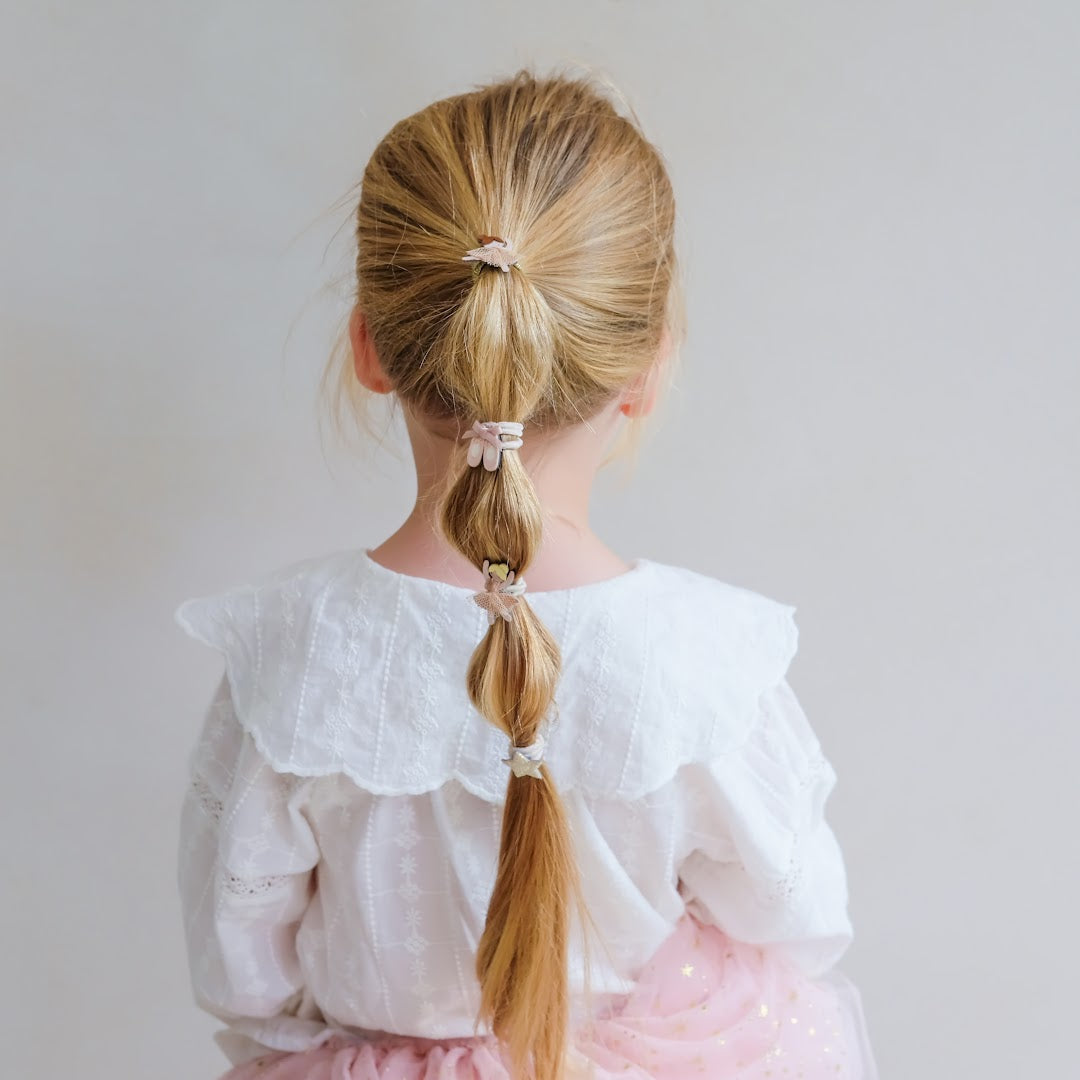 Achterkant van een kind met een blonde vlecht vastgezet met meerdere kleine haarelastiekjes.