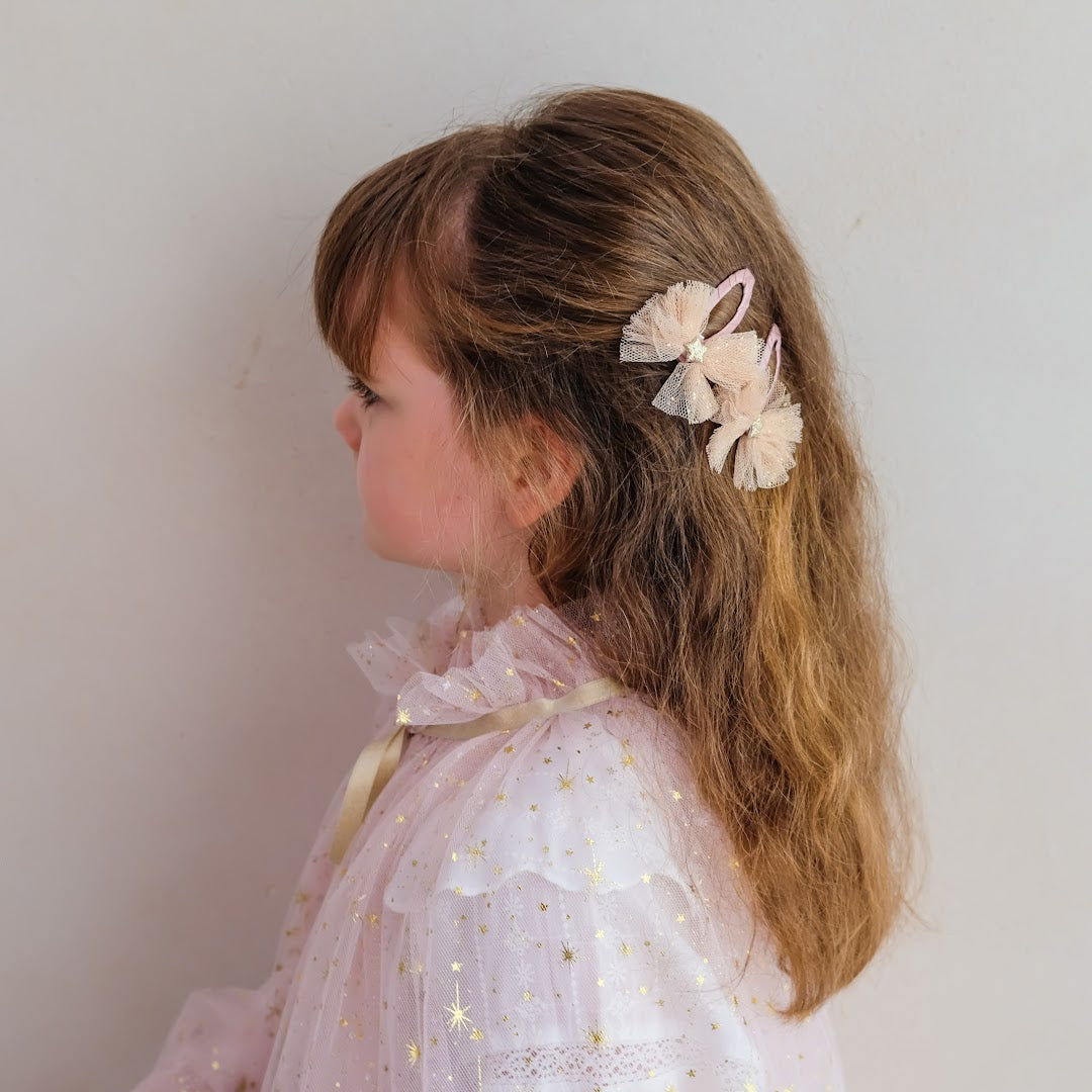 Een kind met lange bruine haren draagt twee mimi & lula haarclipjes met roze tutu strikken.