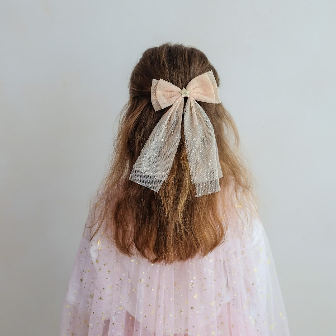 Meisje van achteren met de beige tule haarstrik in haar lange bruine haar.