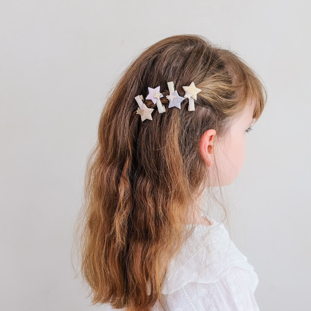 Een kind met lang bruin haar draagt mimi & lula haarclipjes met sterren aan de zijkant van het hoofd.