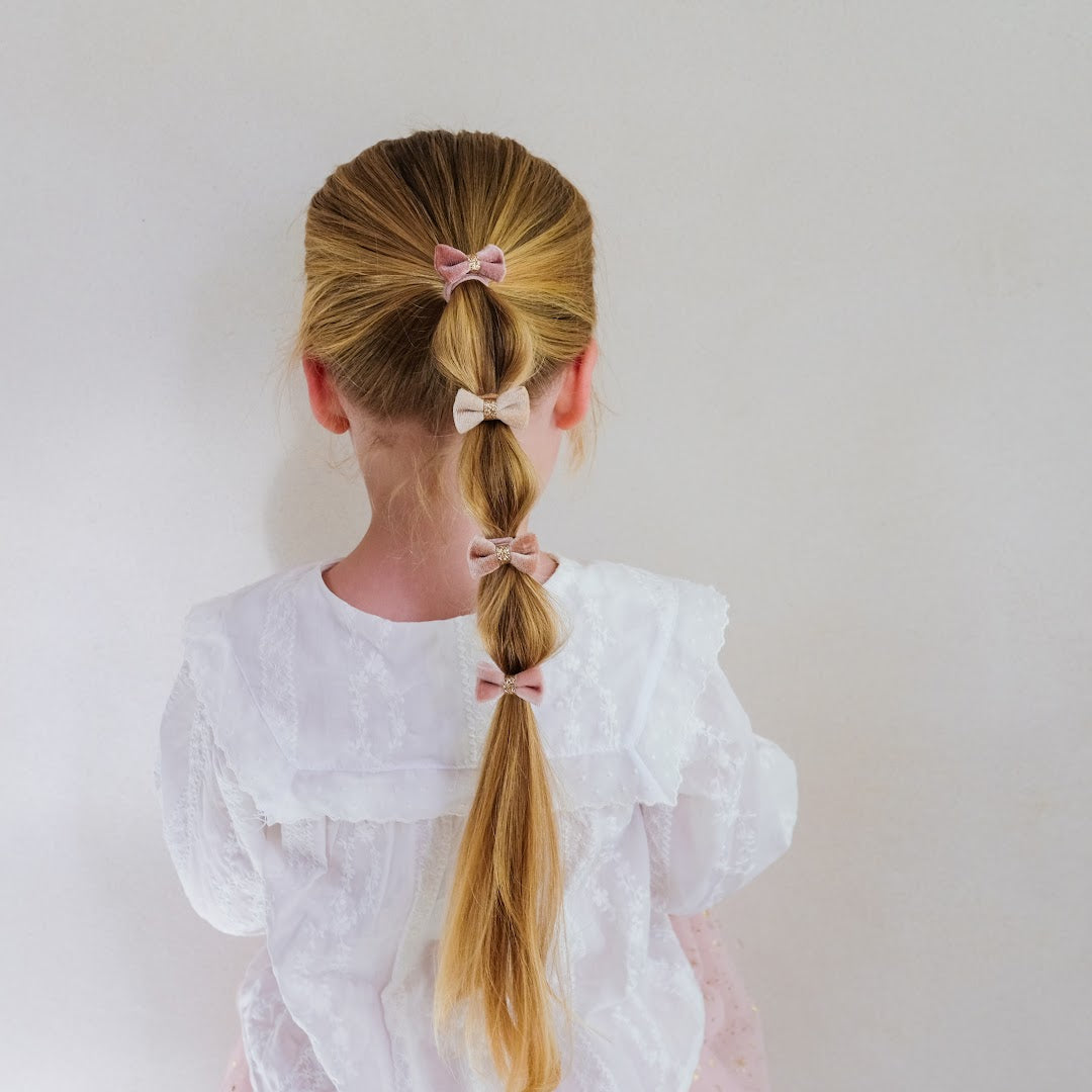 Achterkant van een kind met lang blond haar, versierd met vier mimi & lula fluwelen haarelastiekjes in een vlecht.