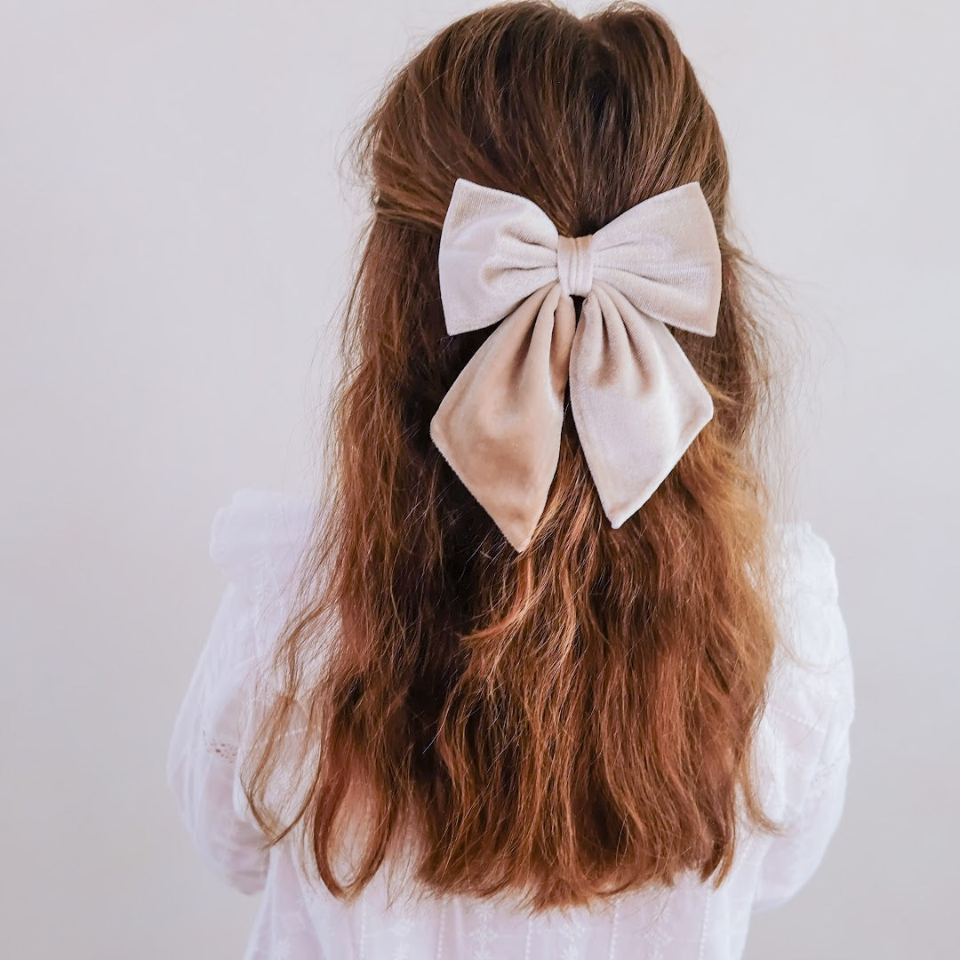 Een meisje met lang bruin haar draagt een grote beige mimi & lula Agnes fluwelen haarstrik.