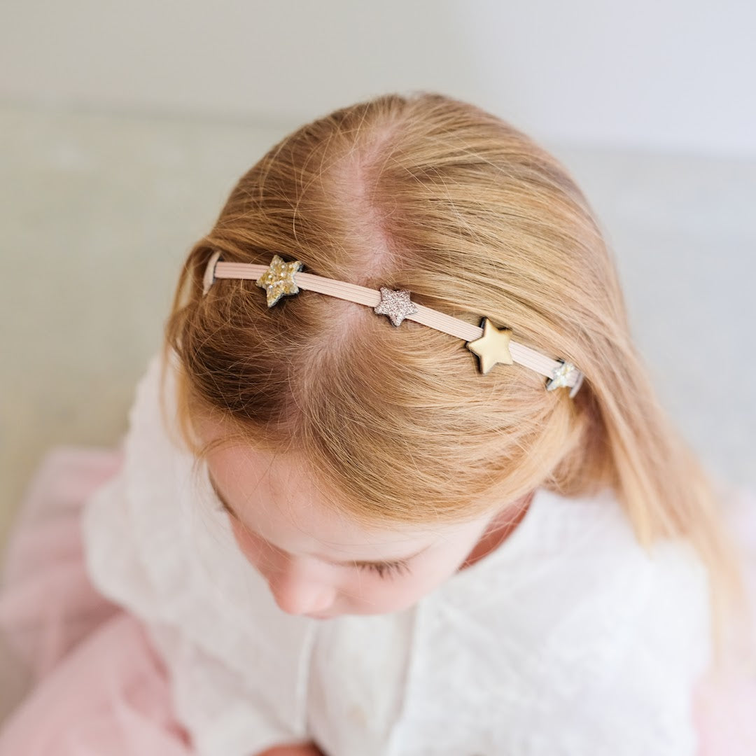 Een kind draagt de mimi & lula haarband met sterren in het blonde haar.