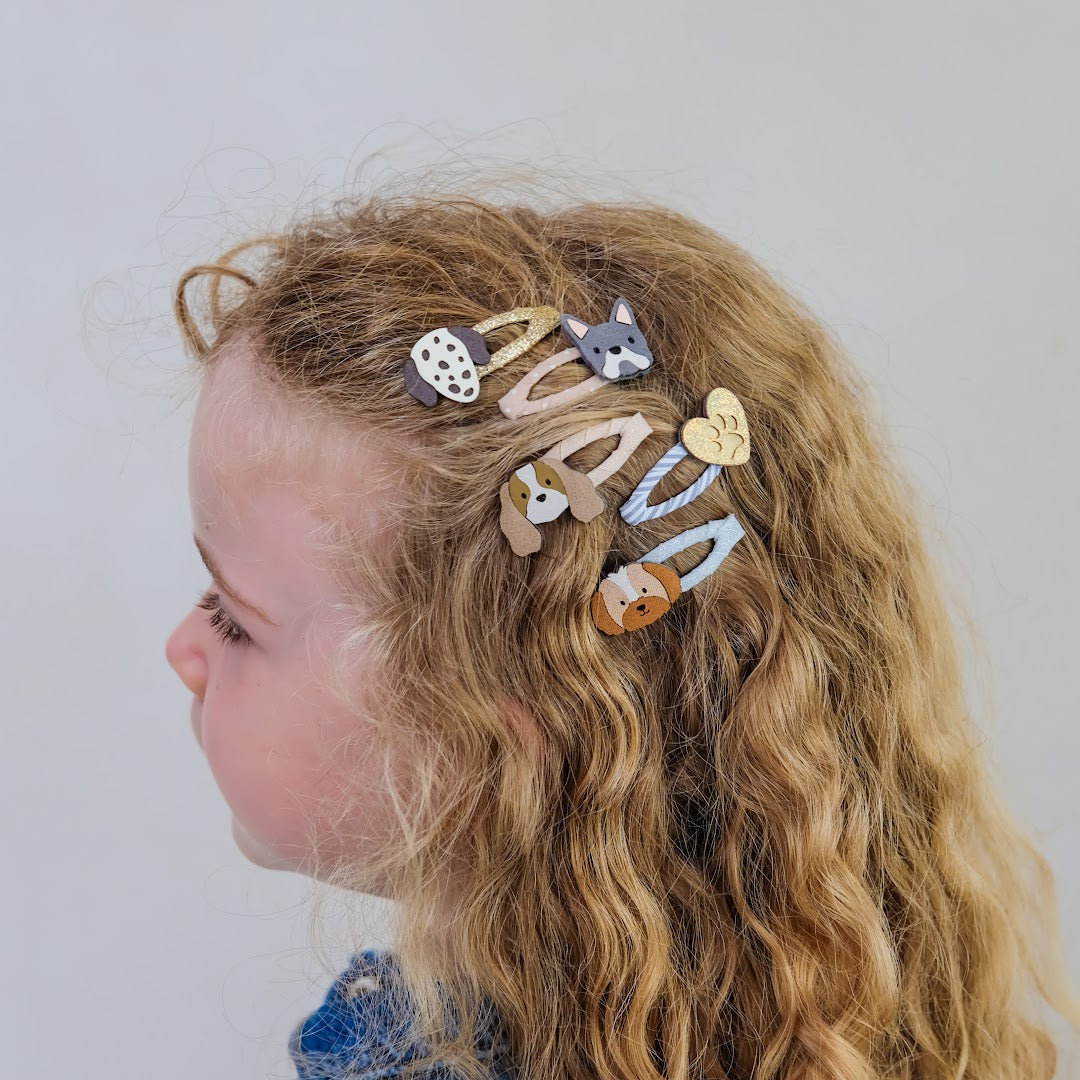 Zijprofiel van een kind met blonde krullen, versierd met Mimi & Lula kinder haarclipjes met honden en een hart.