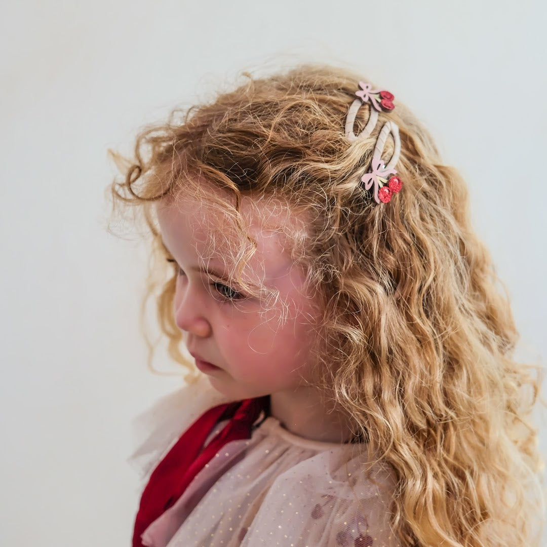 Een meisje met krullend haar draagt twee mimi & lula kinder haarclipjes met kersenmotief.