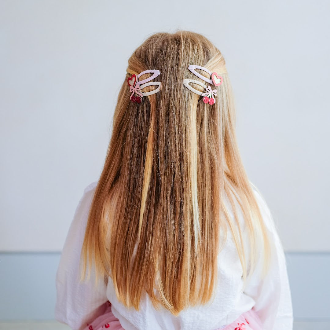 Een meisje met lang haar draagt vier mimi & lula kinder haarclipjes met kersen- en hartmotieven.
