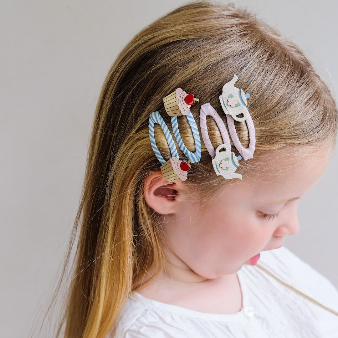 Een kind draagt de Mimi & Lula haarclipjes met theepotjes en cupcakes in haar blonde haar.
