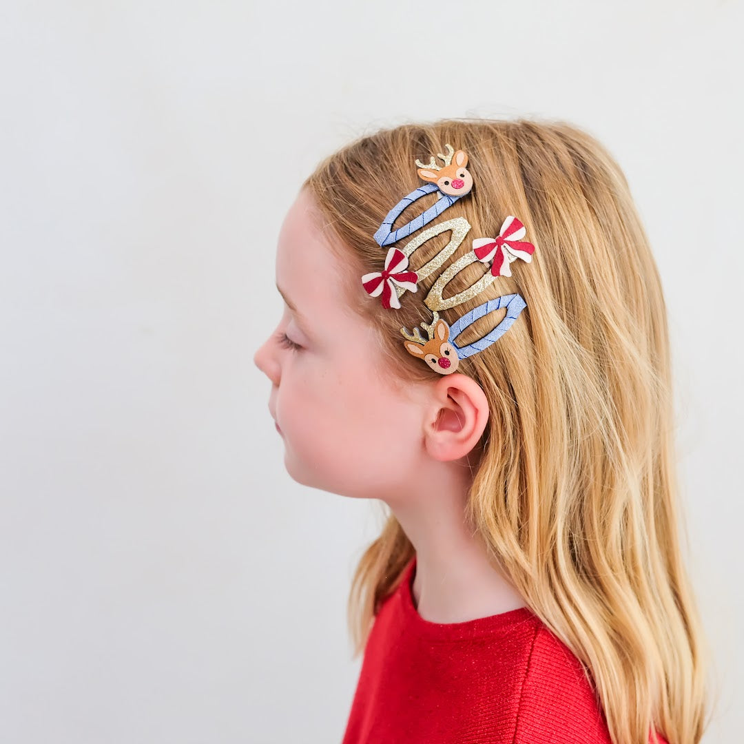 Een kind met blond haar draagt de Rudolph en strikjes haarclipjes aan de zijkant van haar hoofd.