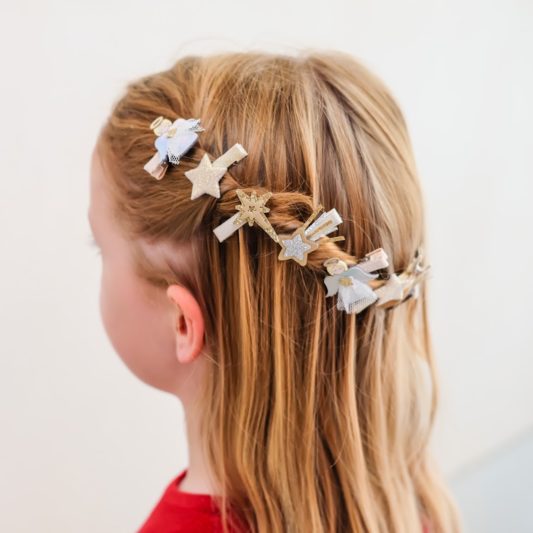 Een kind met blond haar draagt Mimi & Lula haarclipjes met engelen en sterren.