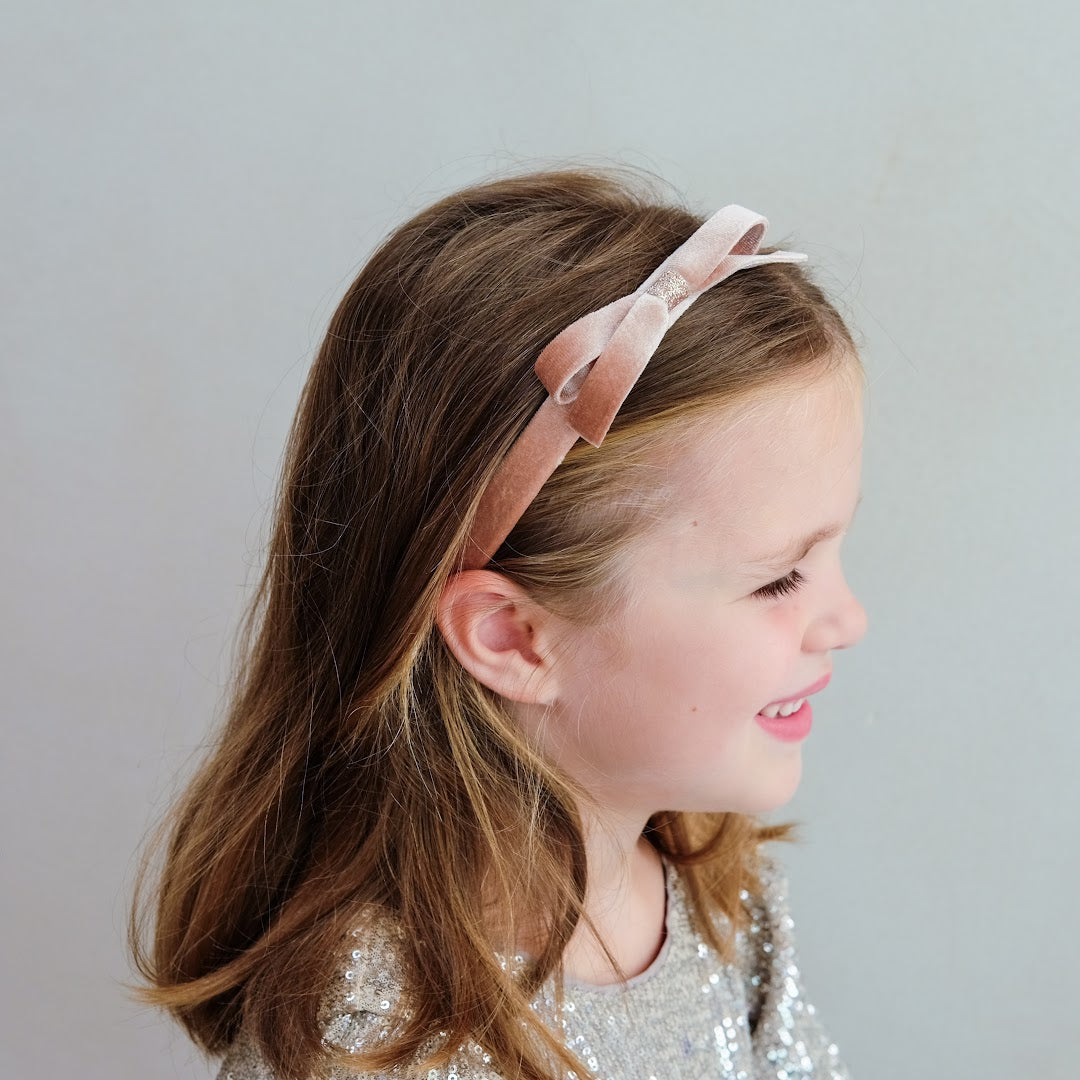 Zijaanzicht van een meisje dat de Mimi & Lula roze fluwelen kinderhaarband draagt.