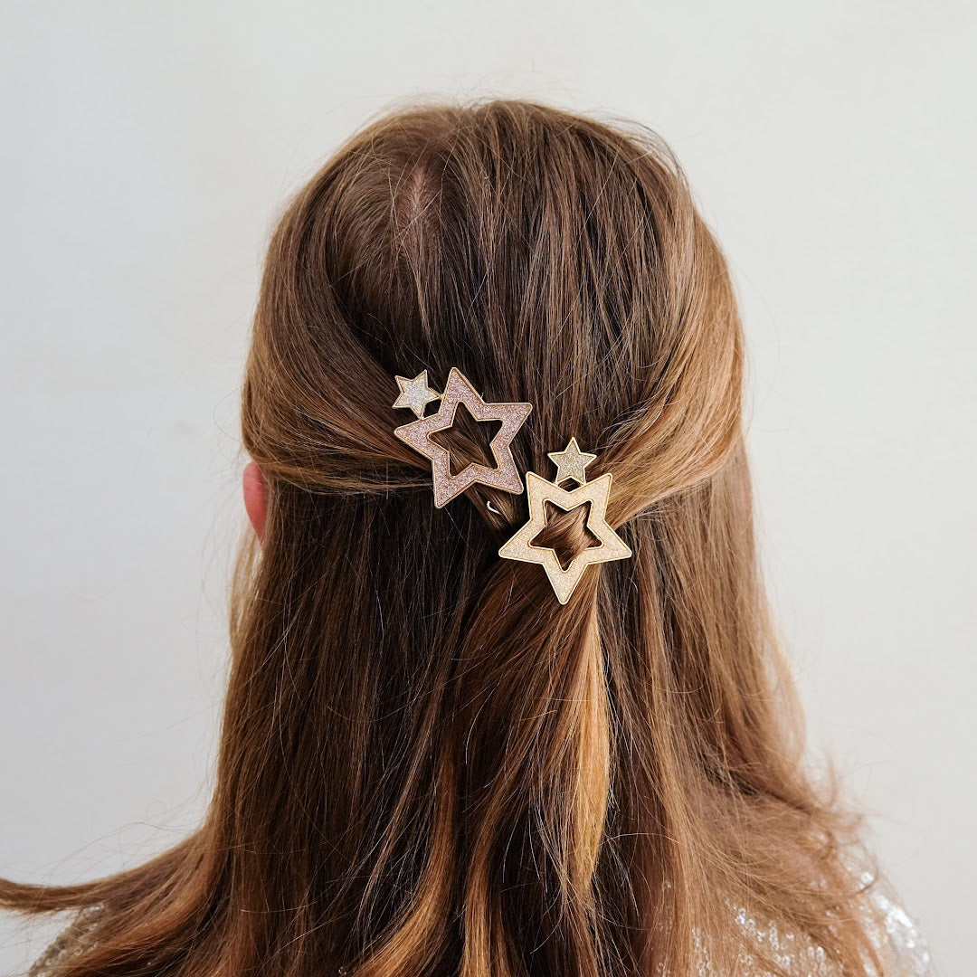 Twee mimi & lula haarclipjes met glittersterren in het bruine haar van een kind, van achteren gefotografeerd.