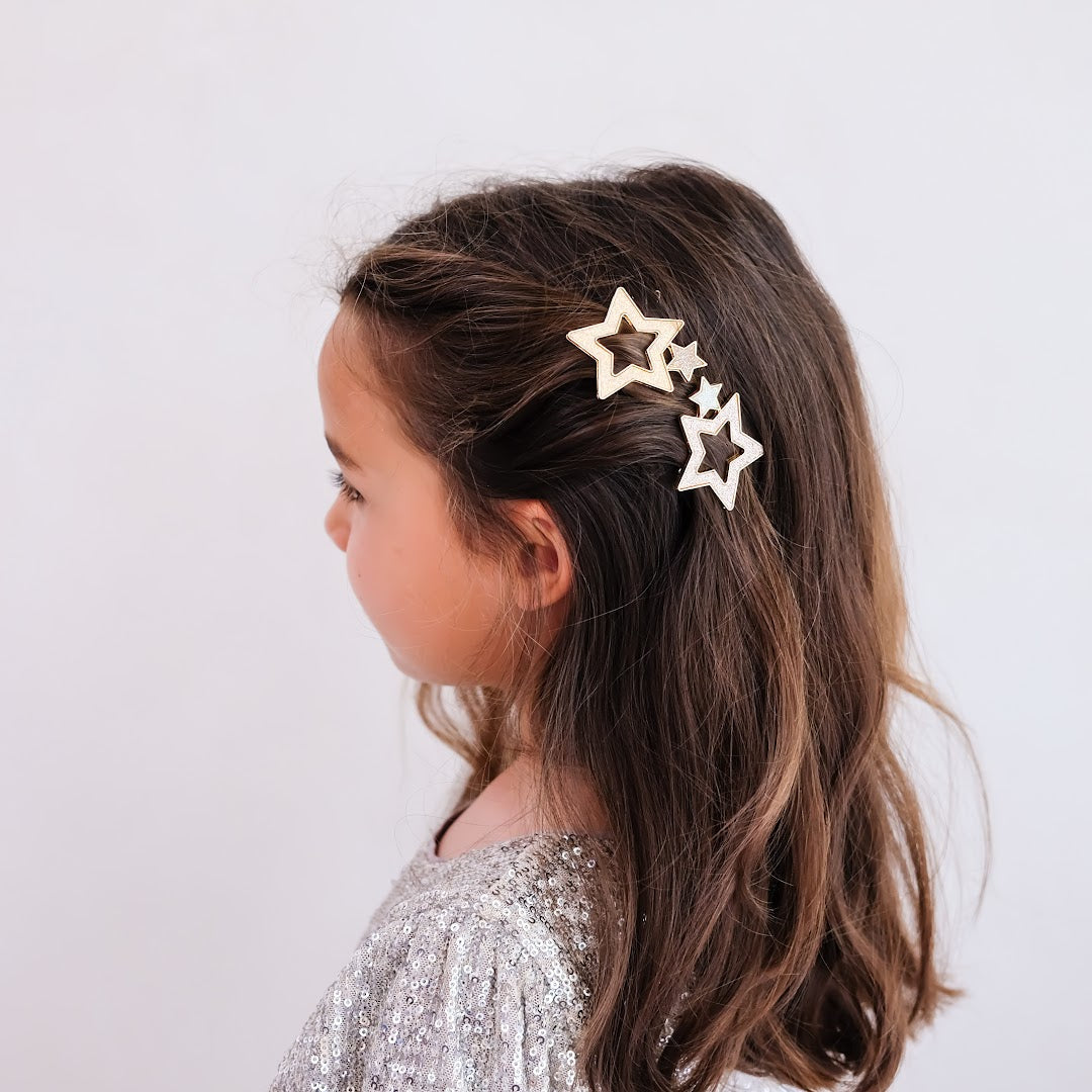 Een kind met bruin haar draagt de twee mimi & lula haarclipjes met glittersterren aan de zijkant van het hoofd.