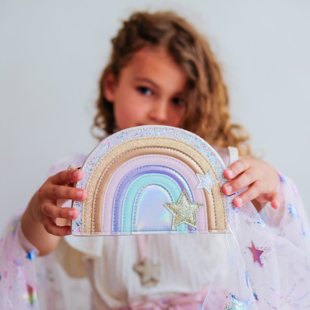 Een kind houdt het mimi & lula regenboog schoudertasje vast.